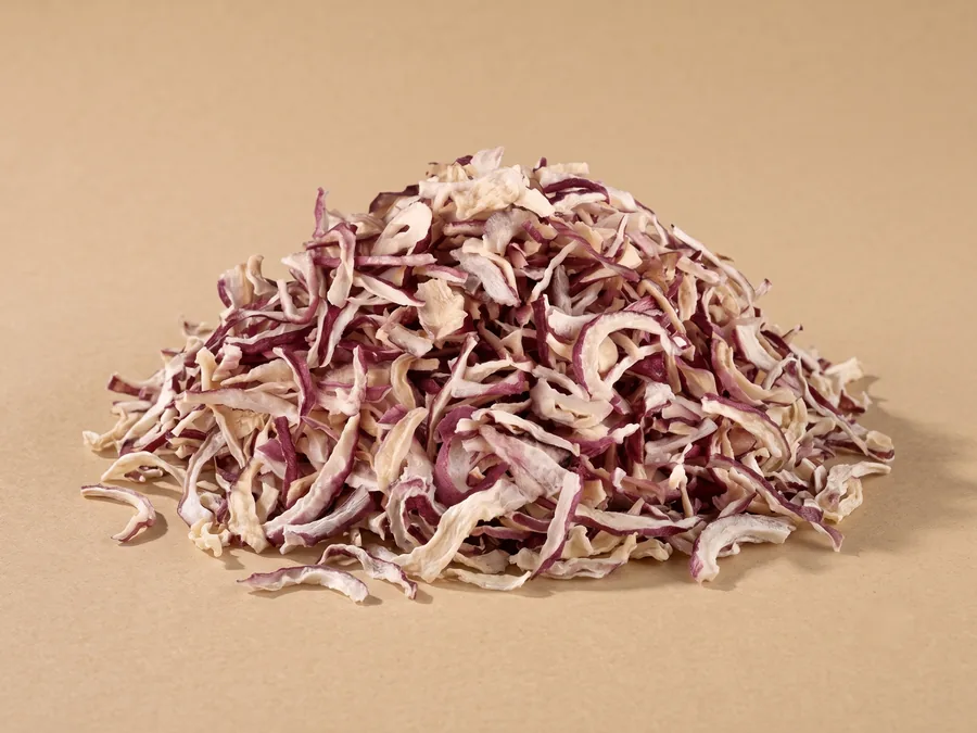 Dehydrated red onion flakes, 8 to 20 mm, cream flesh edged with burgundy skin, in a loose pile on kraft paper.