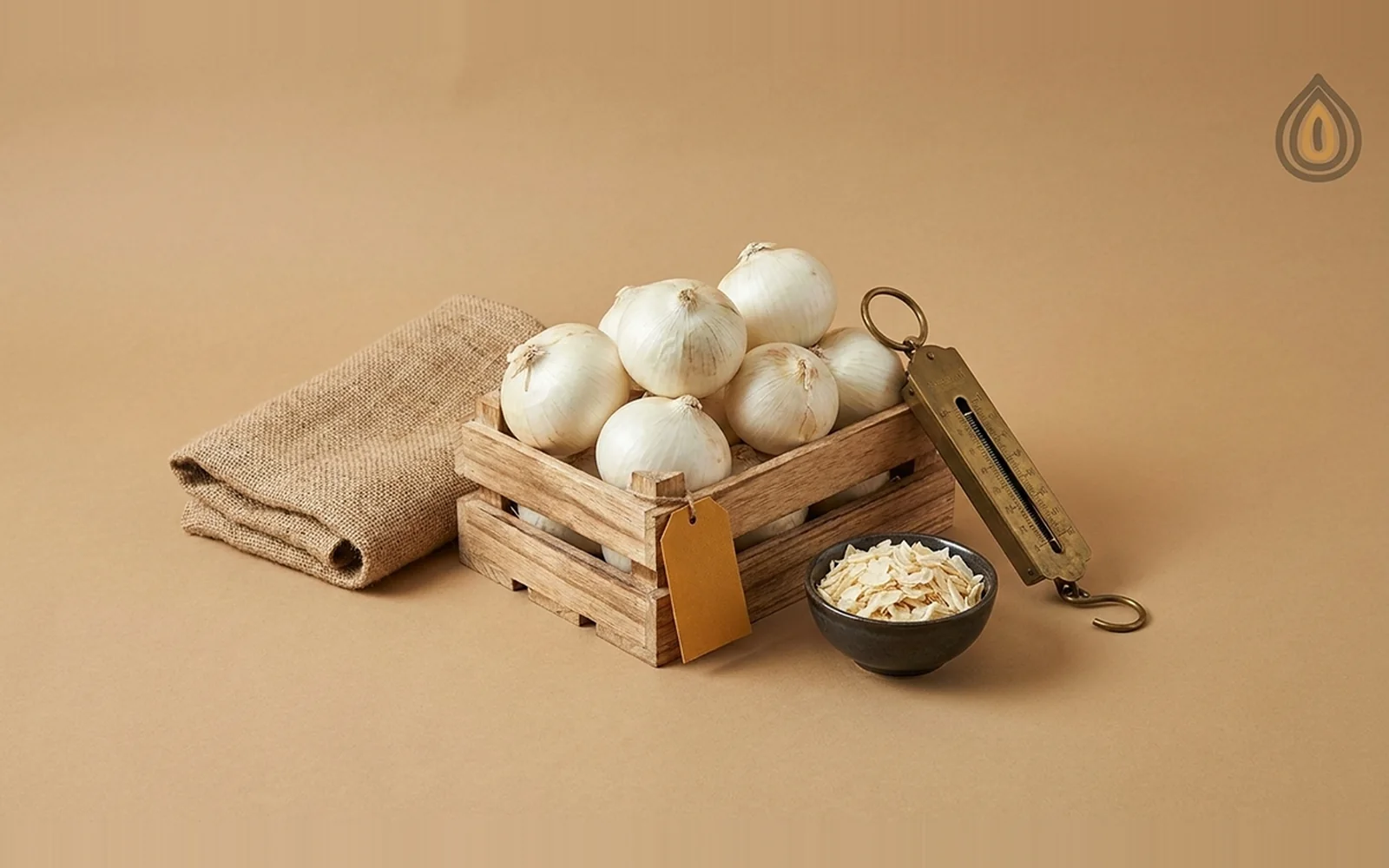 Wooden crate of fresh white onions, a jute sack, a brass hand scale and a bowl of dehydrated onion flakes on a plain backdrop