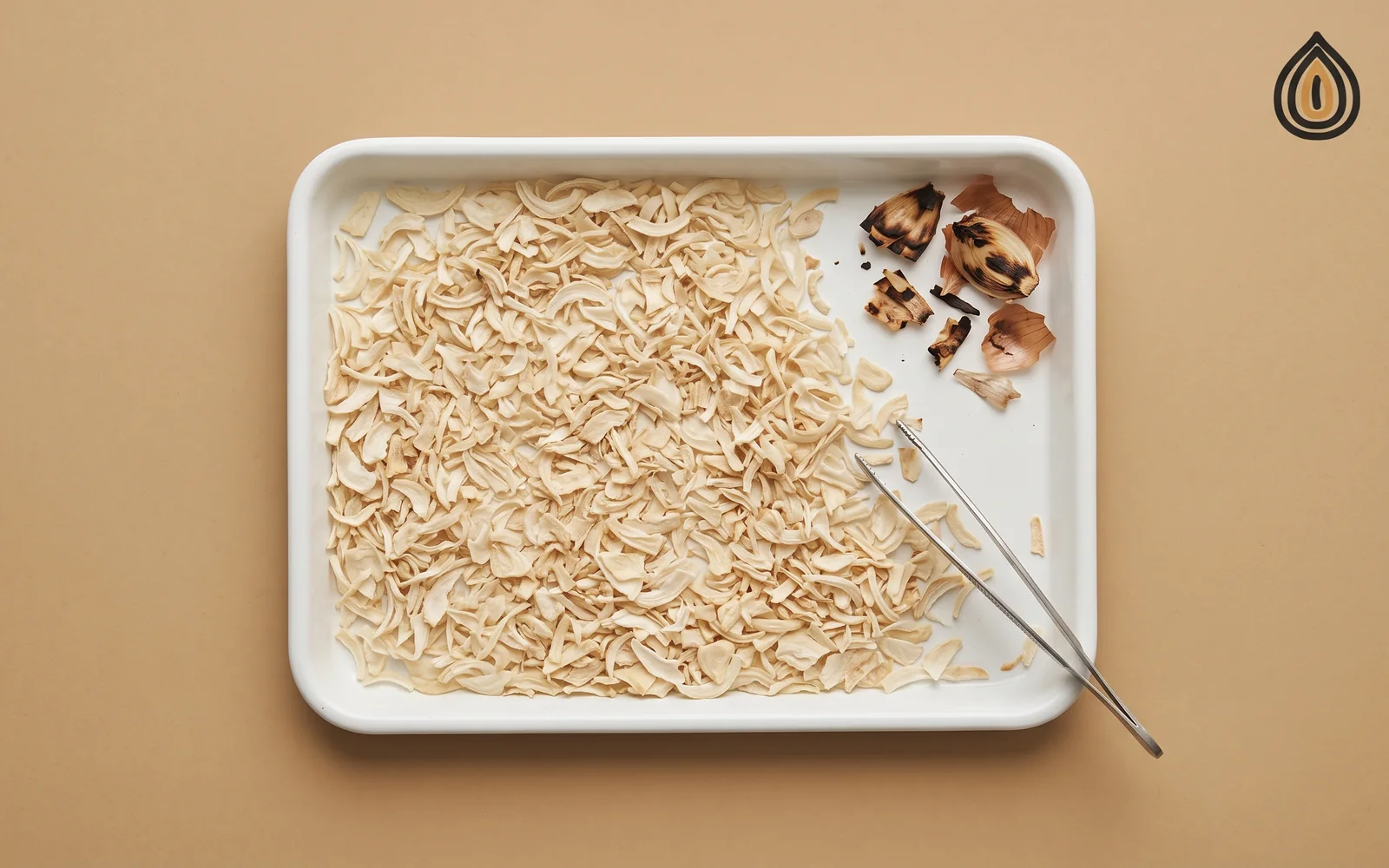 White tray of dehydrated onion flakes with a few dark scorched pieces and skin fragments picked out to one side with tweezers