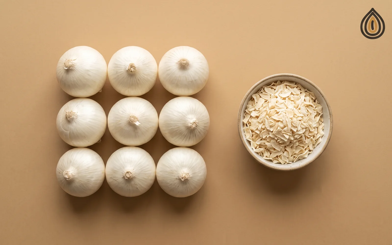 Nine fresh white onions in a row beside one small bowl of dehydrated onion flakes on a wooden board
