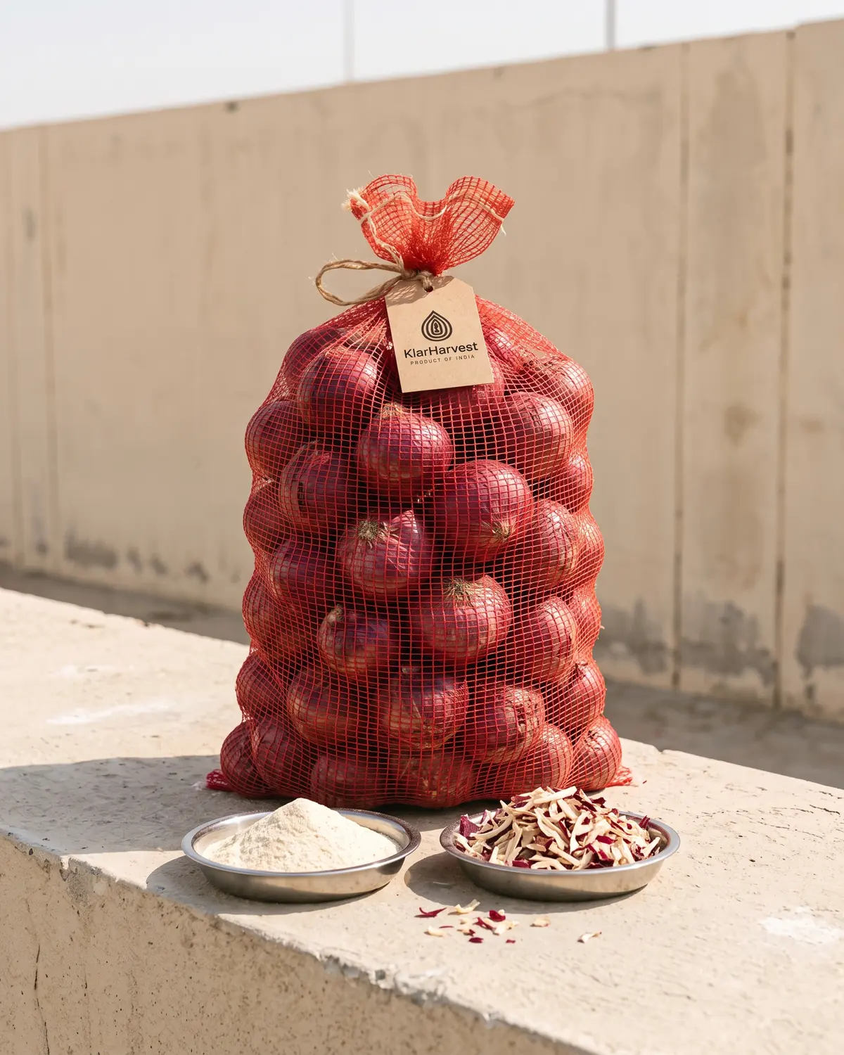 A red mesh bag of fresh red onions with a kraft tag standing in bright sunlight beside dishes of white onion powder and red onion flakes.