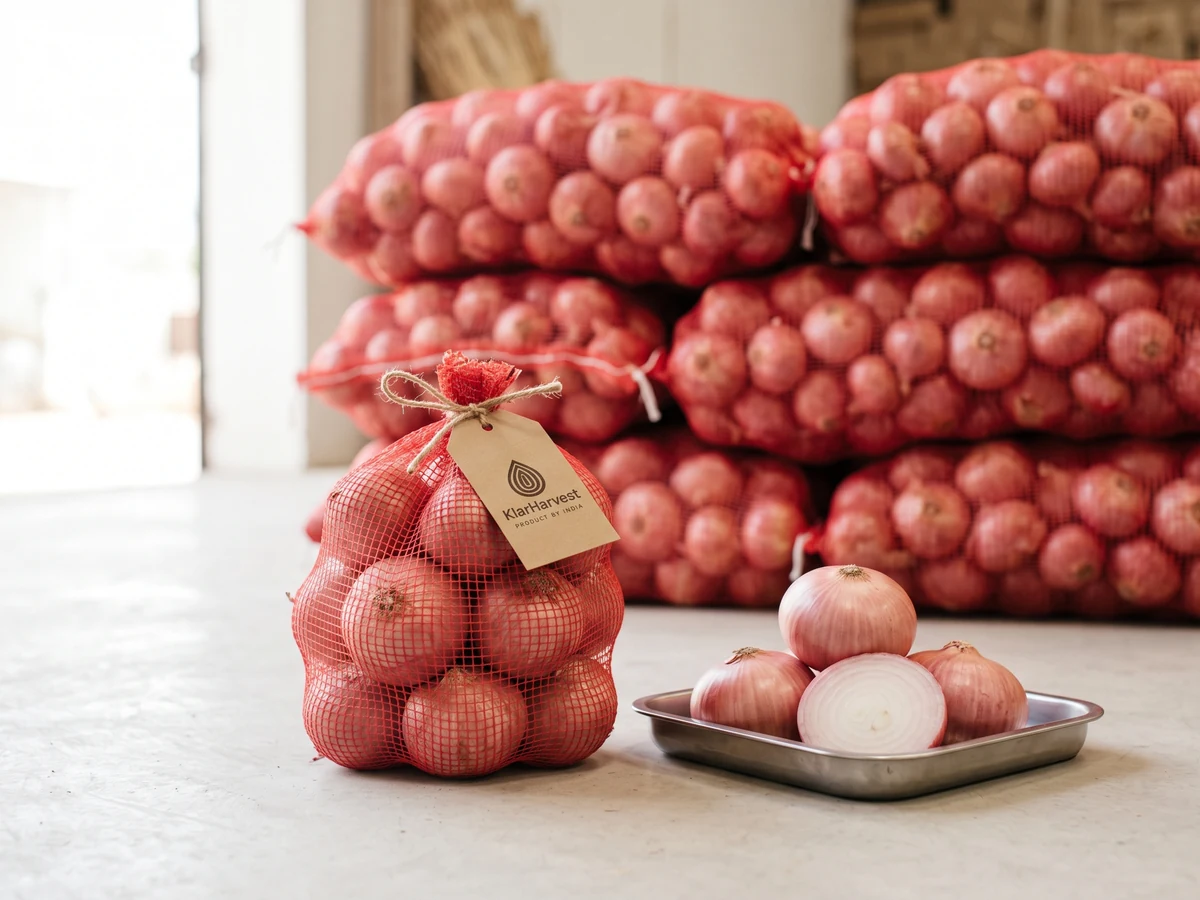 A small clipped mesh bag of fresh pink onions with a KlarHarvest kraft tag in front of a stack of large mesh bags, loose bulbs and a cut half on a tray.